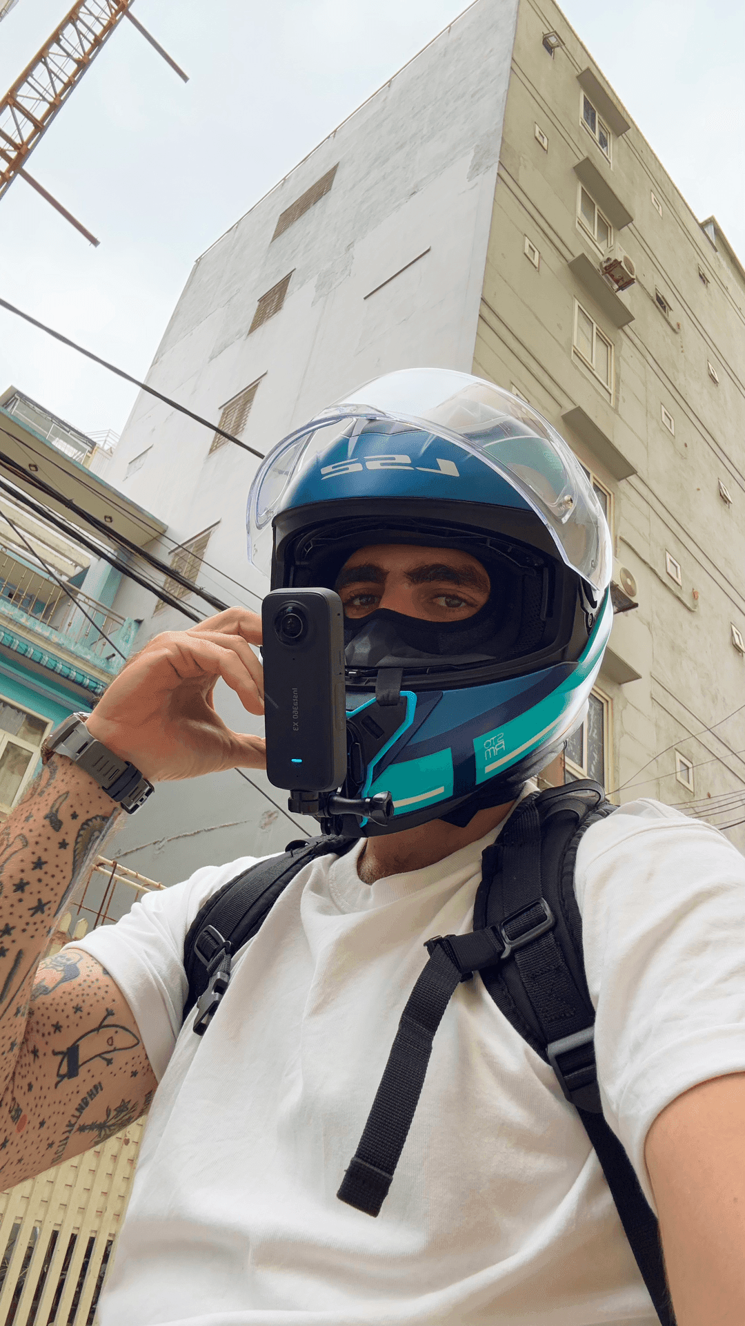 Person wearing a motorcycle helmet with a camera attached, standing in front of a tall building.