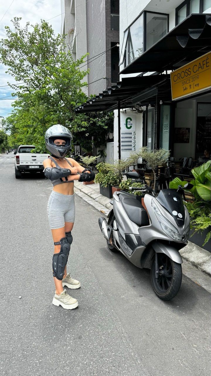 Person in protective gear standing next to a parked scooter outside Cross Café on a city street.